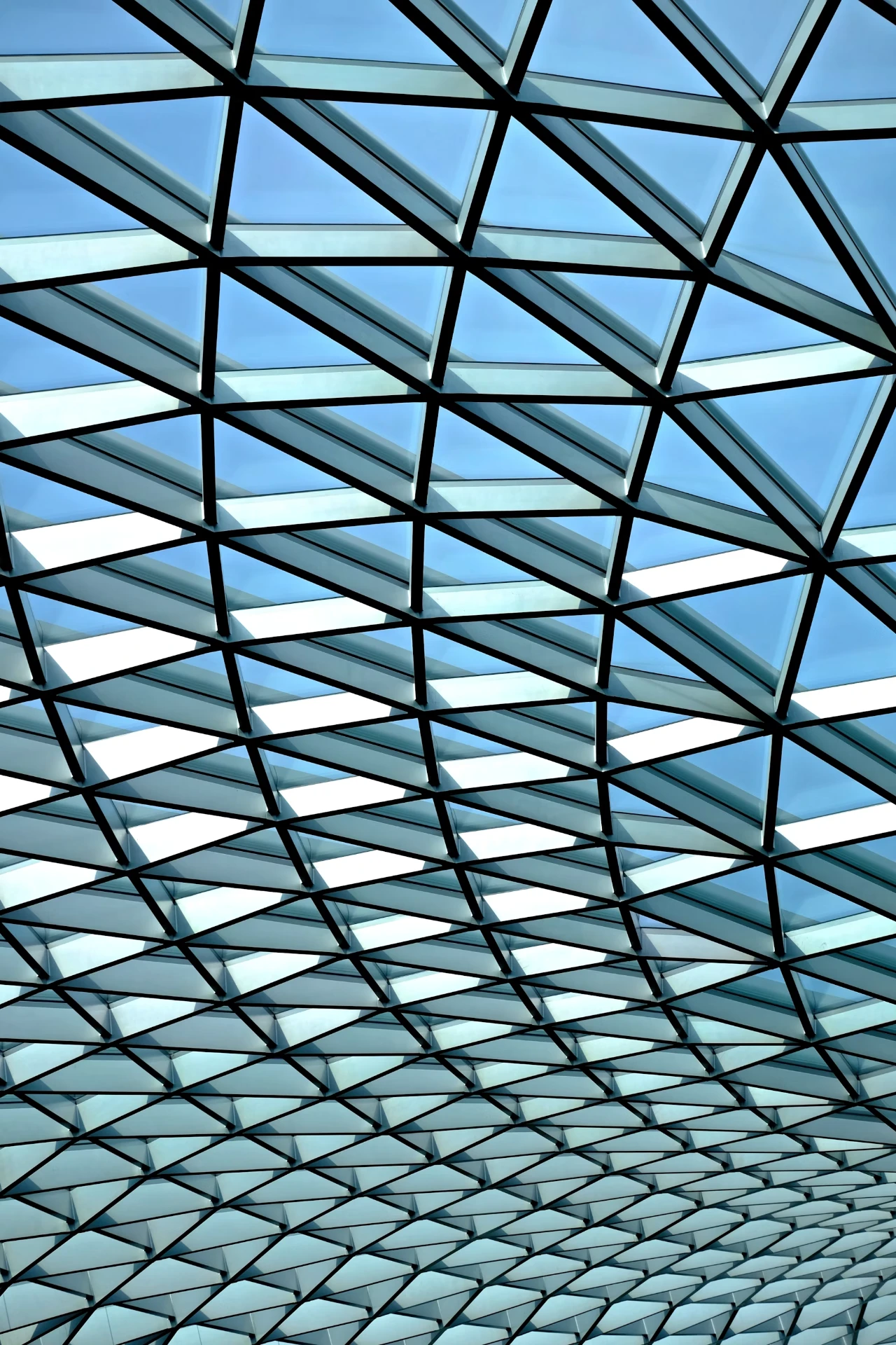Verrière géométrique en verre et acier vue d'en dessous, ciel bleu.