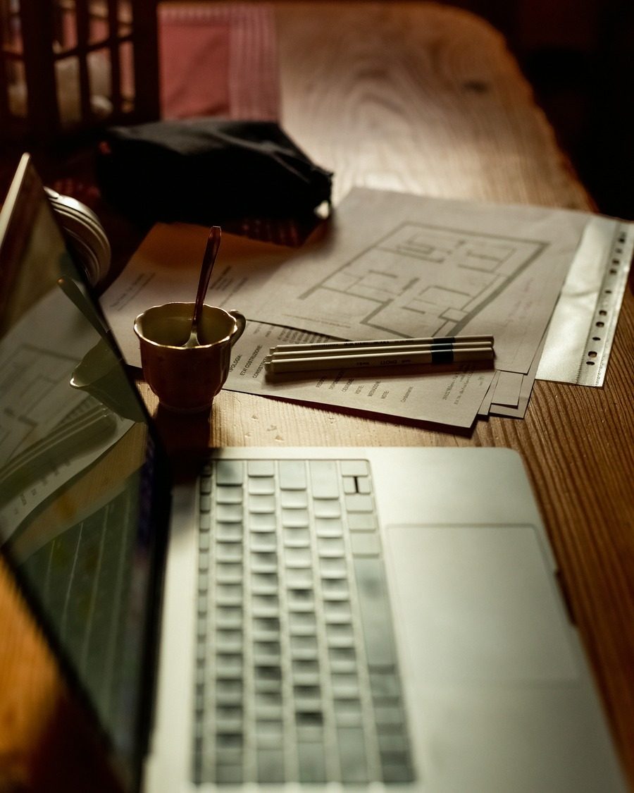 Bureau en bois, ordinateur portable et plans posés à côté d'un café.